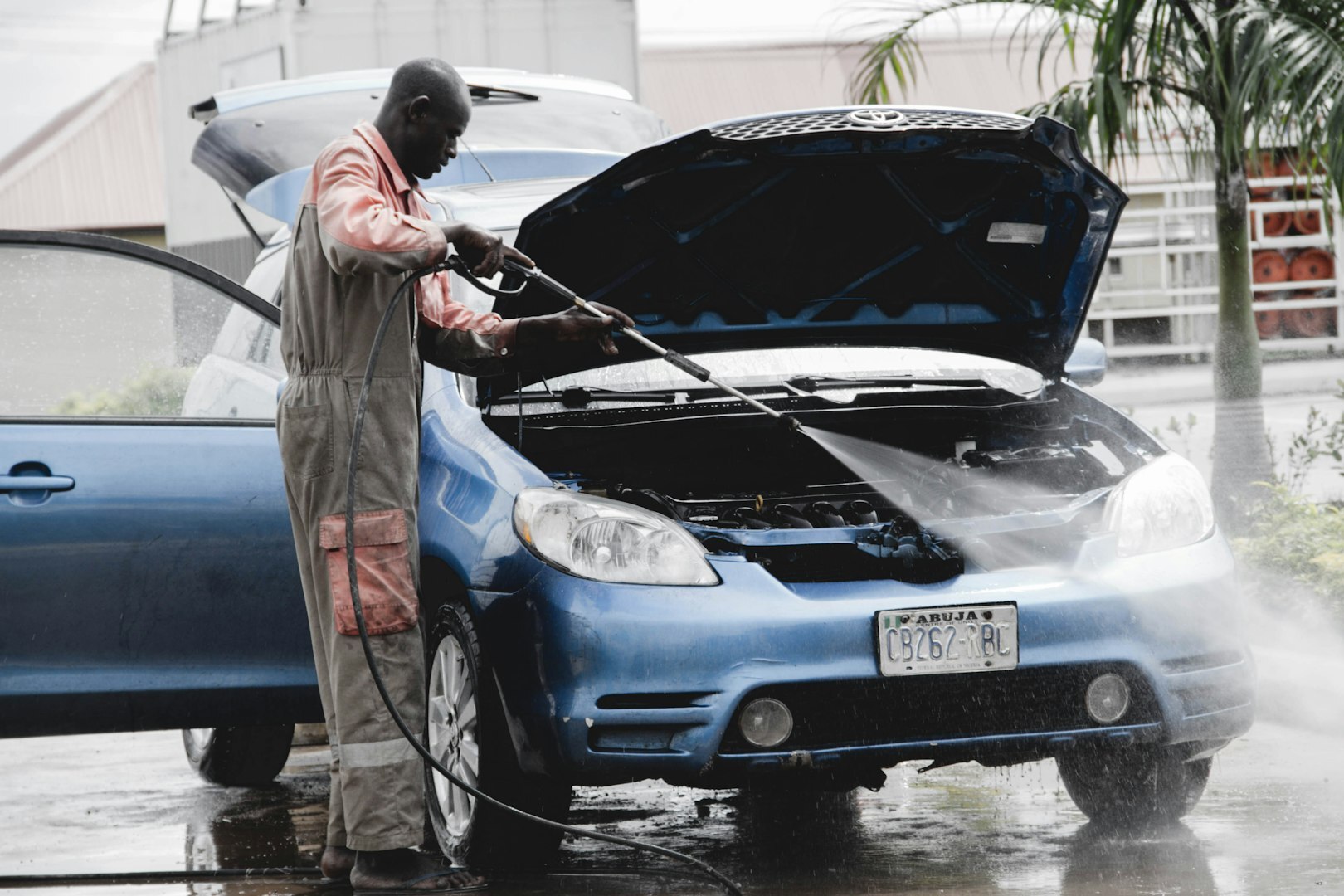 man in gray coat standing beside blue car during daytime man in gray coat standing beside blue car during daytime