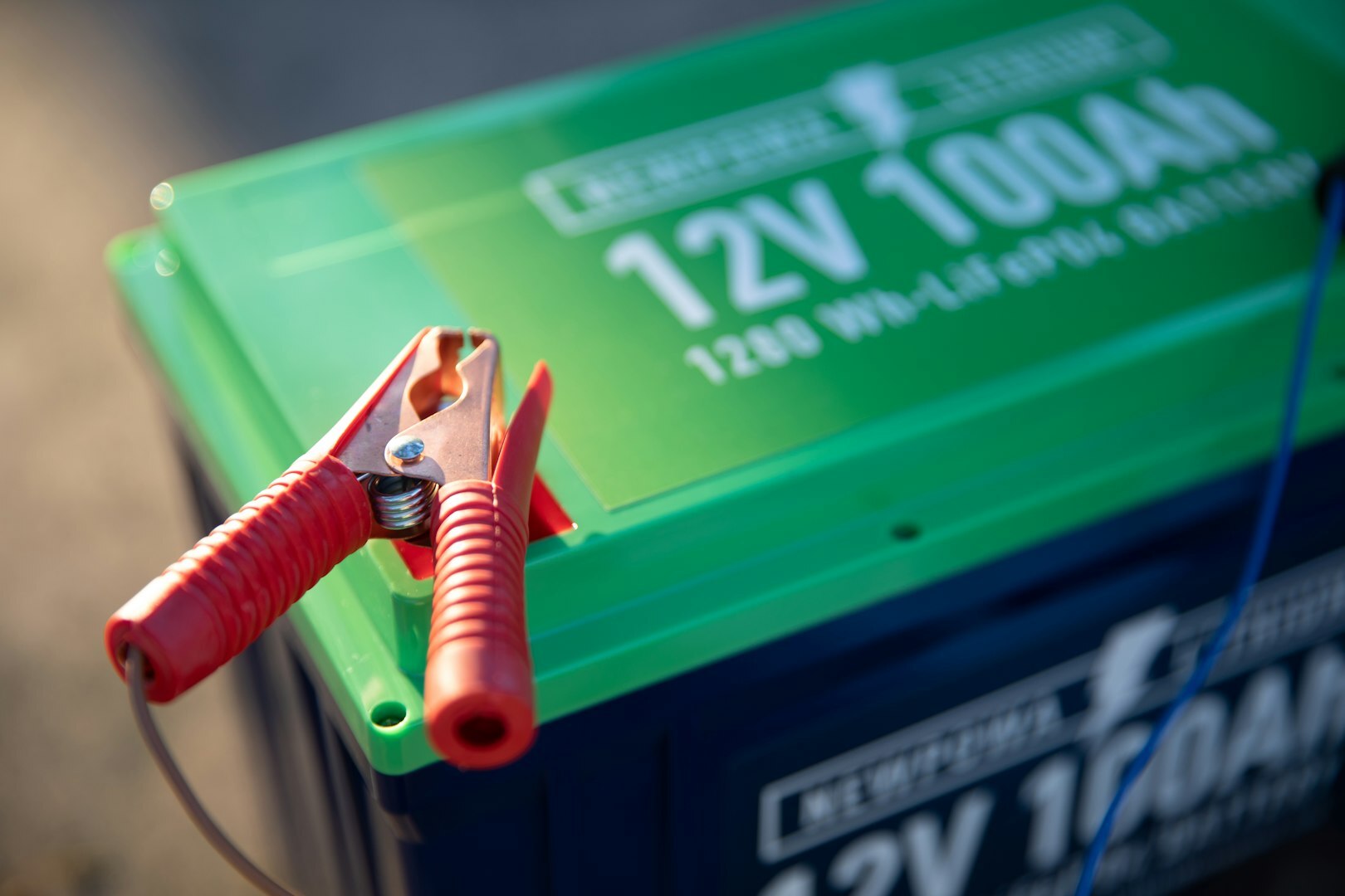 akumulator samochodowy a red and green battery with a pair of pliers attached to it
